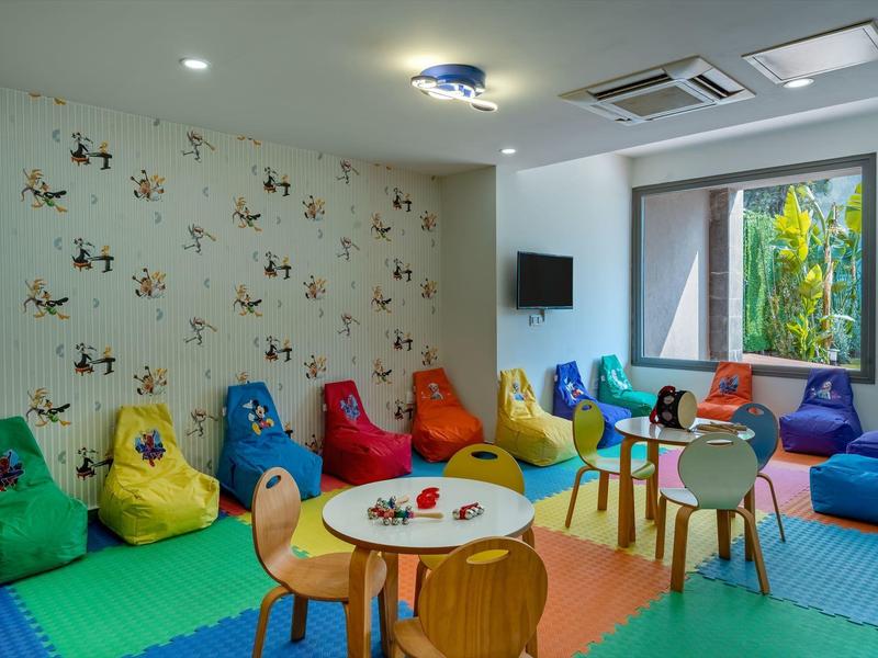Kolorowa sala zabaw dla dzieci z matami, workowymi fotelami i stołami z krzesłami.