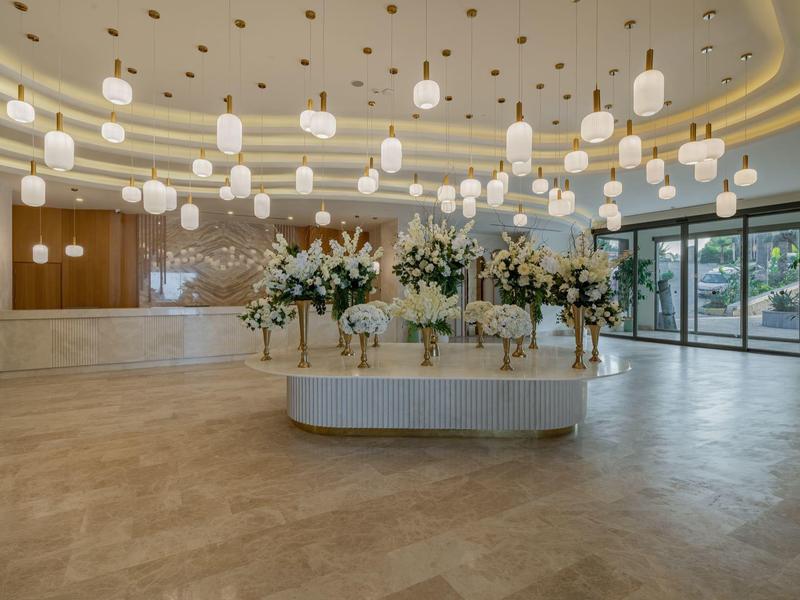 Przestronne lobby hotelowe z nowoczesnym wystrojem i białymi kwiatami na stołach.