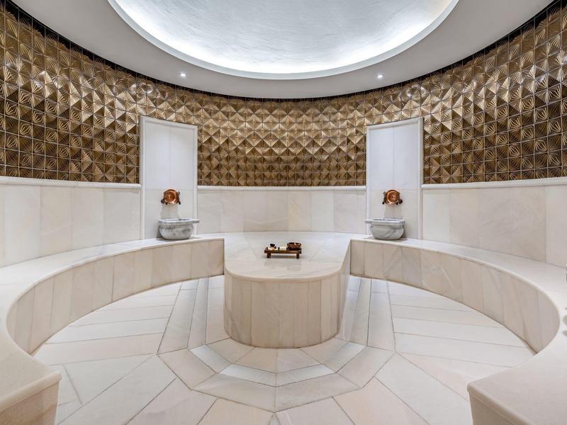 Okrągły salon spa z ozdobionymi ścianami i zintegrowanymi kamiennymi siedzeniami.