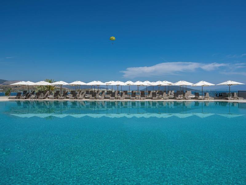 Basen na zewnątrz z białymi parasolami i leżakami pod jasnoniebieskim niebem.