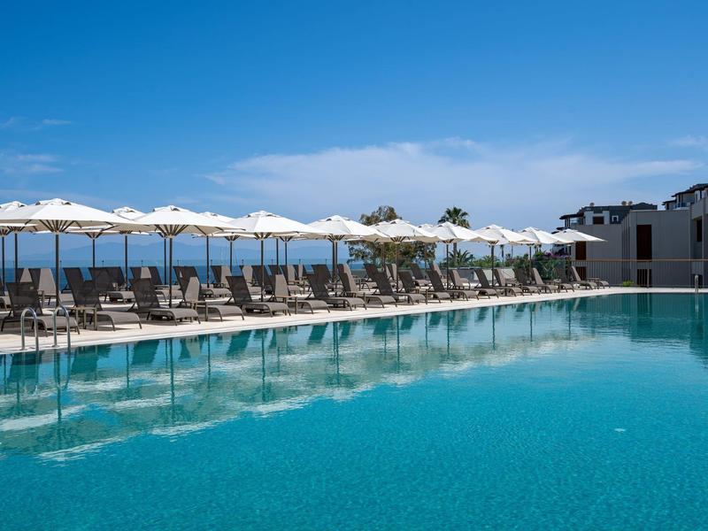 Basen z leżakami i parasolami pod bezchmurnym, niebieskim niebem.