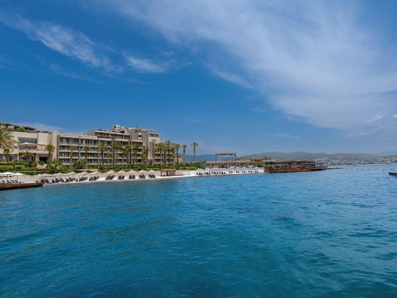 Widok na hotel przy plaży z parasolami i turkusową wodą.