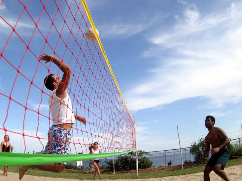 Ludzie grający w siatkówkę na plaży pod częściowo pochmurnym niebem.