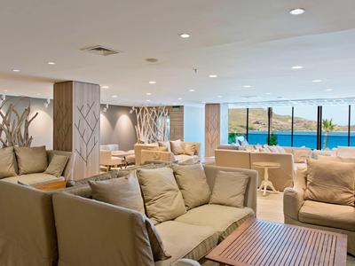 Sala de estar amplia y moderna con sofás beige y vista al mar a través de grandes ventanas.