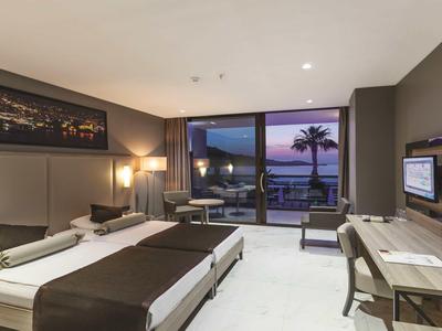 Habitación de hotel moderna con dos camas individuales, escritorio y vista al mar al anochecer.