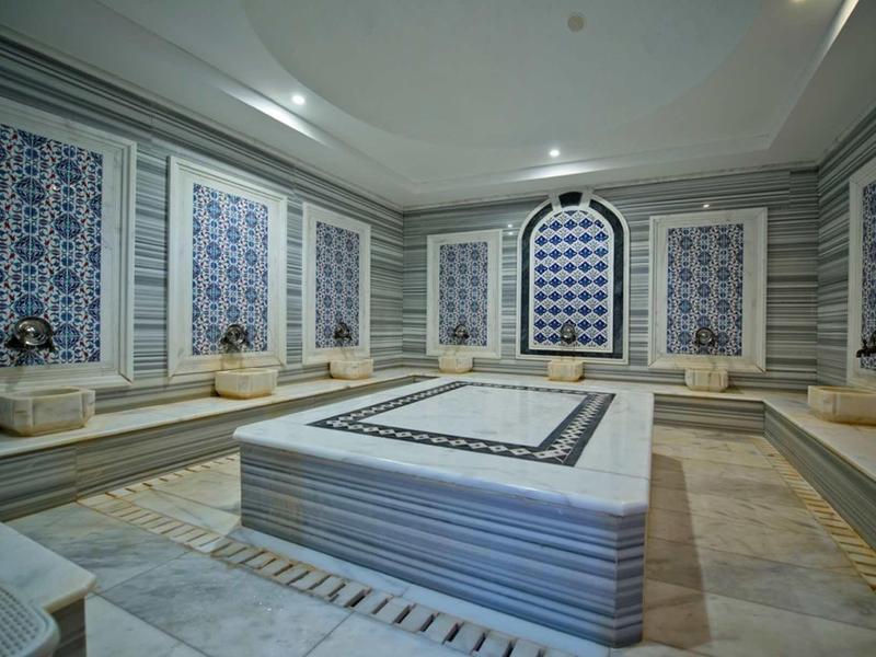 Sala de Hamam tradicional con pila de mármol, asientos y paredes decoradas en hotel.