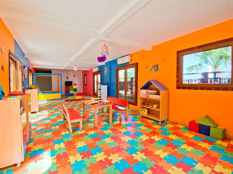 Sala de juegos para niños colorida con alfombrillas de rompecabezas, mesas y juguetes, paredes naranjas claras.