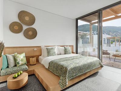 Modern hotel room with large bed, seating bench, and terrace with mountain view.