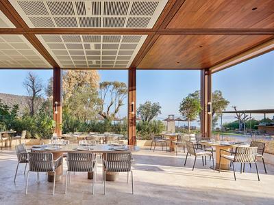 Outdoor dining area with modern tables and chairs under wooden and glass roof.