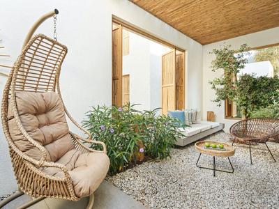 Cozy outdoor area with rattan chair, plants, and seating on stone flooring.