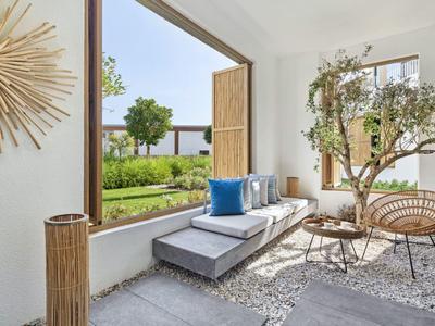 Bright lounge area with plants, wooden decor, and view of garden and blue sky.