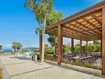 Covered outdoor area with tables and chairs beside a walkway overlooking the sea.