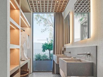 Modern hotel bathroom with open closet, concrete sinks, and large window overlooking plants.