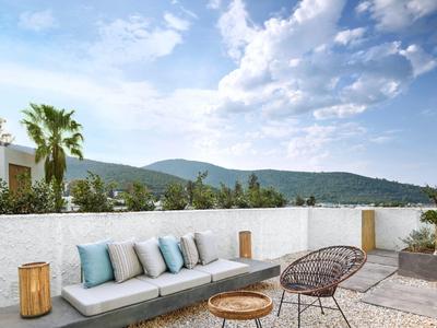 Modern outdoor terrace with sofa, chair, table, and view of green hills under blue sky.