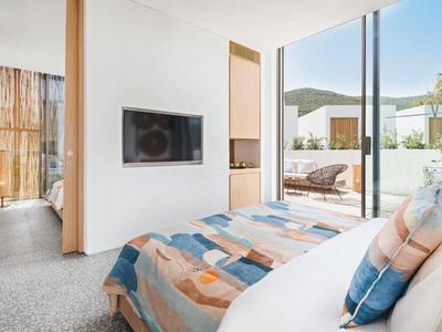 Bright hotel room with bed, wall-mounted TV, and access to terrace overlooking outdoor area.