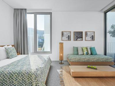 Modern hotel room with two beds, wooden bench, and large window with curtains.