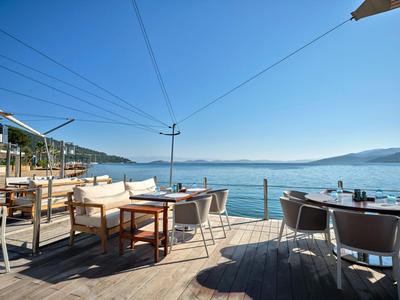 Open terrace with tables and chairs overlooking calm sea and clear sky.