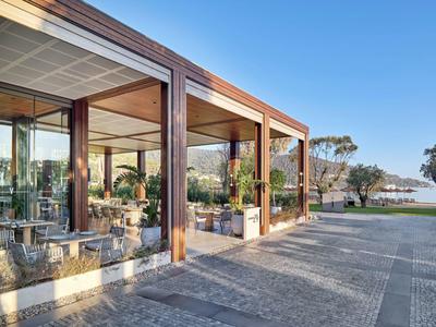 Modern pavilion with wooden frame and glass walls next to an open plaza and blue sky.