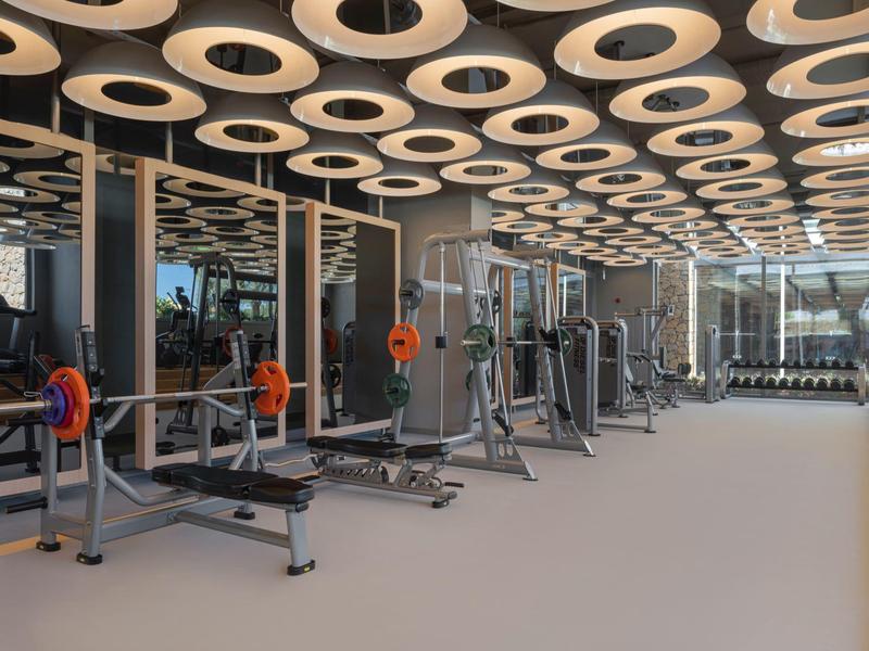 Modern gym with equipment and unique ceiling lighting in a hotel.