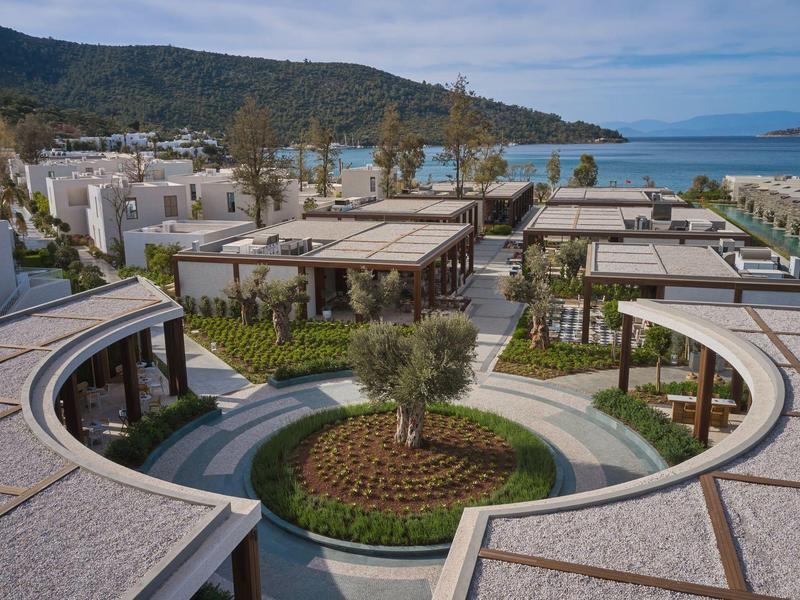 Luxury resort with pavilions, pool, and views of the sea and mountains under clear sky.