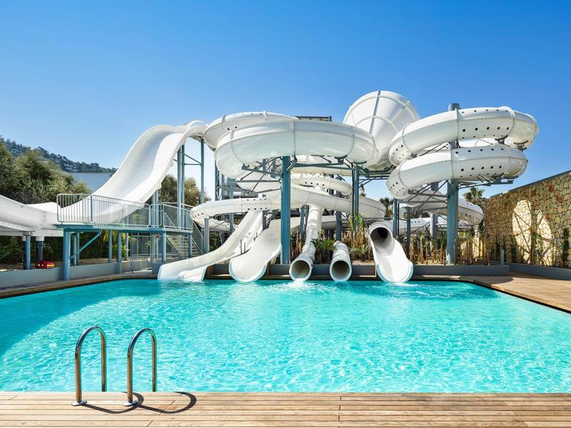 Water slides with multiple chutes next to a clear pool under a blue sky.