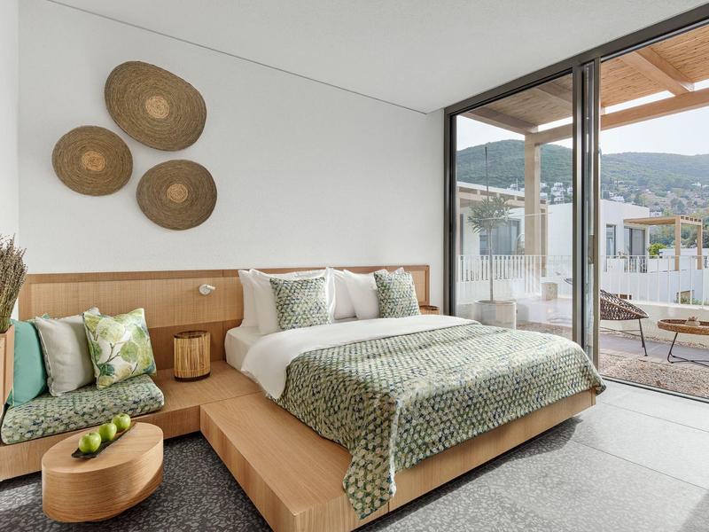 Modern hotel room with large bed, seating bench, and terrace with mountain view.