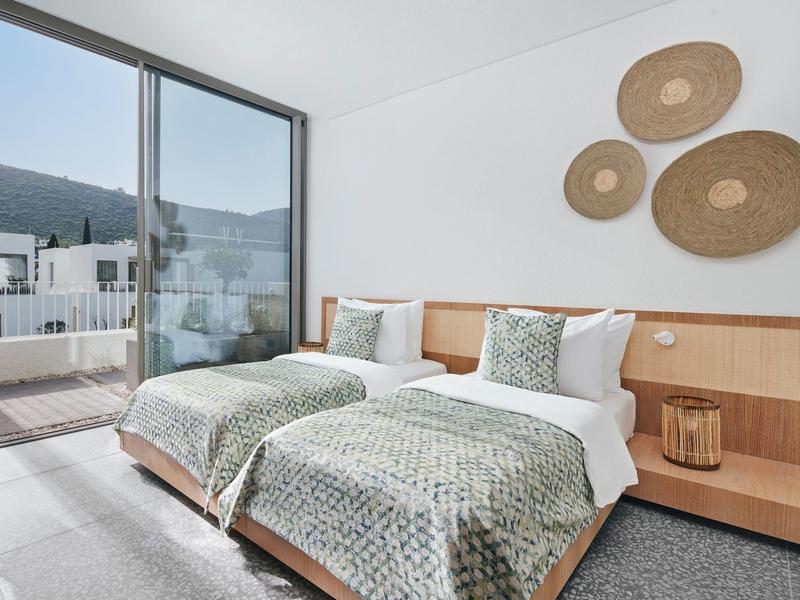 Bright twin room with two beds, modern wood decor, and balcony access with mountain view.