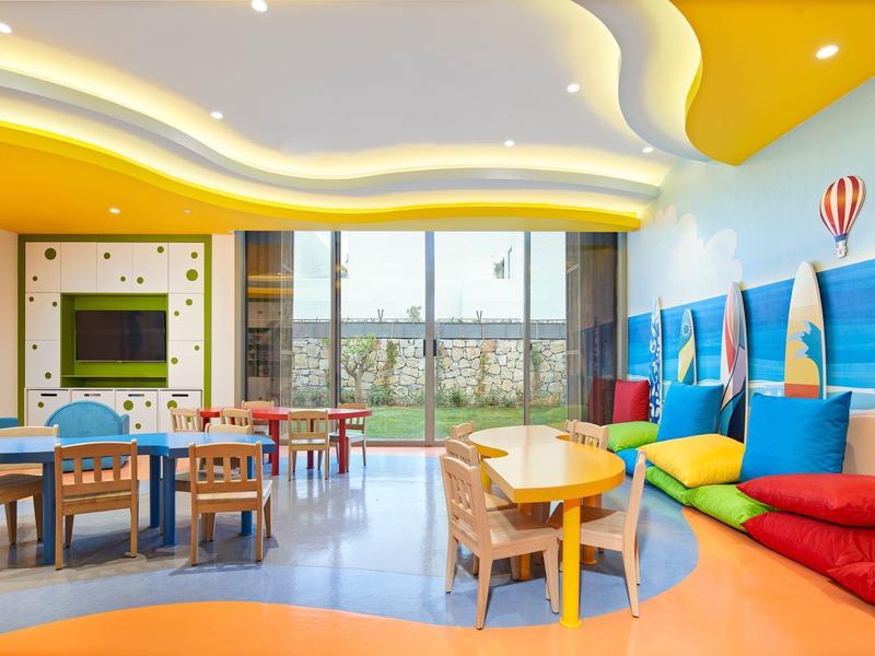 Bright playroom with colorful chairs, tables, and soft cushions next to large windows.
