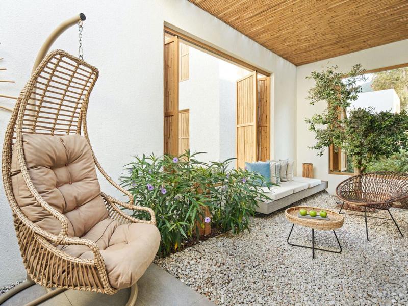 Cozy outdoor area with rattan chair, plants, and seating on stone flooring.