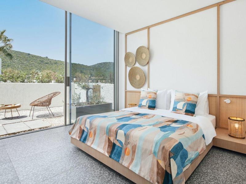 Bright bedroom with large bed, terrace doors, and outdoor seating area with mountain view.