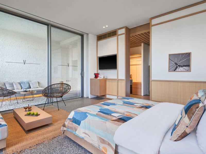 Modern hotel room with large bed, wood paneling, and balcony with seating area.