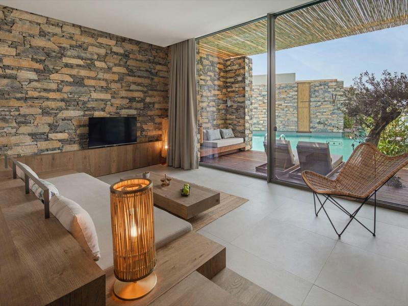 Modern hotel room with stone wall, large windows, and view of terrace and pool.