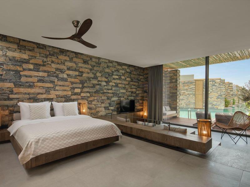 Modern bedroom with large bed, natural stone wall, and terrace overlooking mountains.