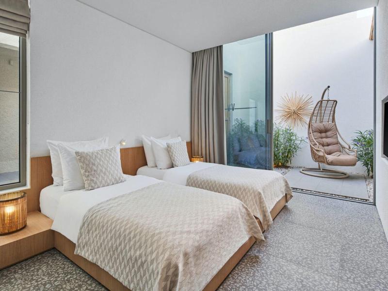 Modern hotel room with two single beds and view of terrace with hanging chair.