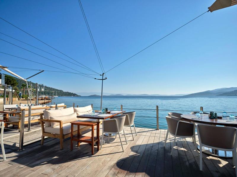Open terrace with tables and chairs overlooking calm sea and clear sky.