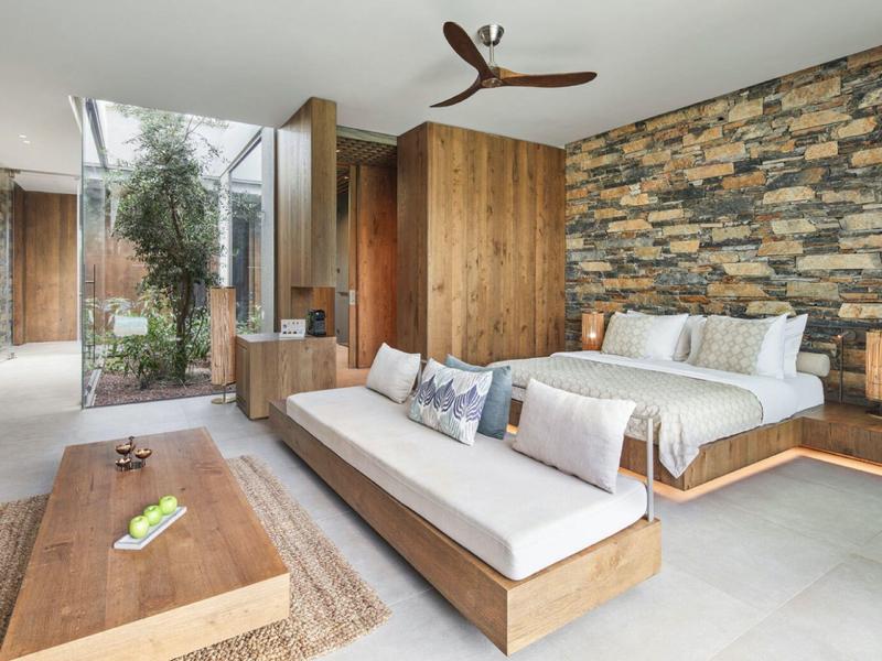 Modern hotel room with stone wall, wood paneling, cozy bed, and seating area.