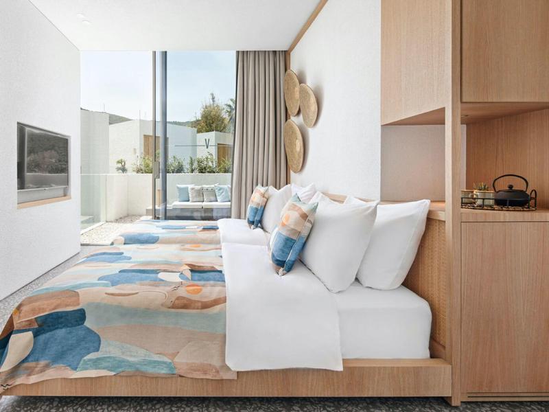 Modern double room with light wood, colorful rug, and floor-to-ceiling windows with balcony