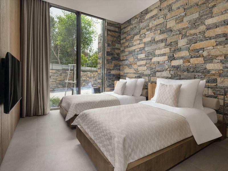 Modern hotel room with two beds, stone walls, and garden view.