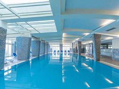 Large modern indoor pool with white columns and blue water in a hotel.