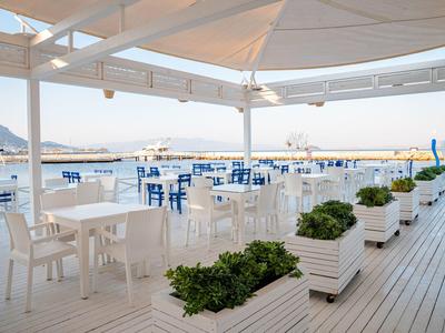 Open area of a beach restaurant with white tables and chairs, overlooking the sea.