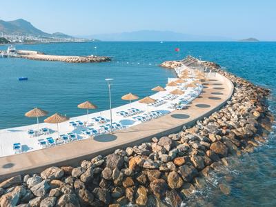 Dlouhá zakřivená molo s lehátky a slunečníky u čistého modrého moře.