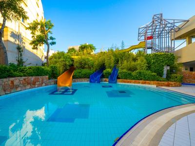 Klares Außenbecken mit Wasserrutschen in einer Hotelanlage unter blauem Himmel.