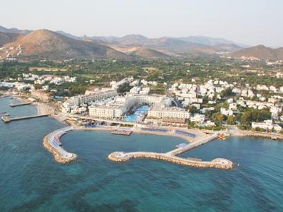 Aerial view of a coastal town with harbor, beaches, and mountains in the background.