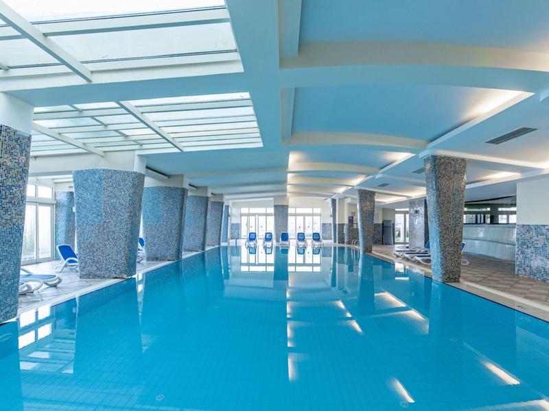 Large modern indoor pool with white columns and blue water in a hotel.