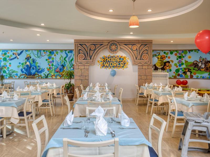 Bright restaurant with blue tablecloths and large colorful underwater-themed wall decoration.