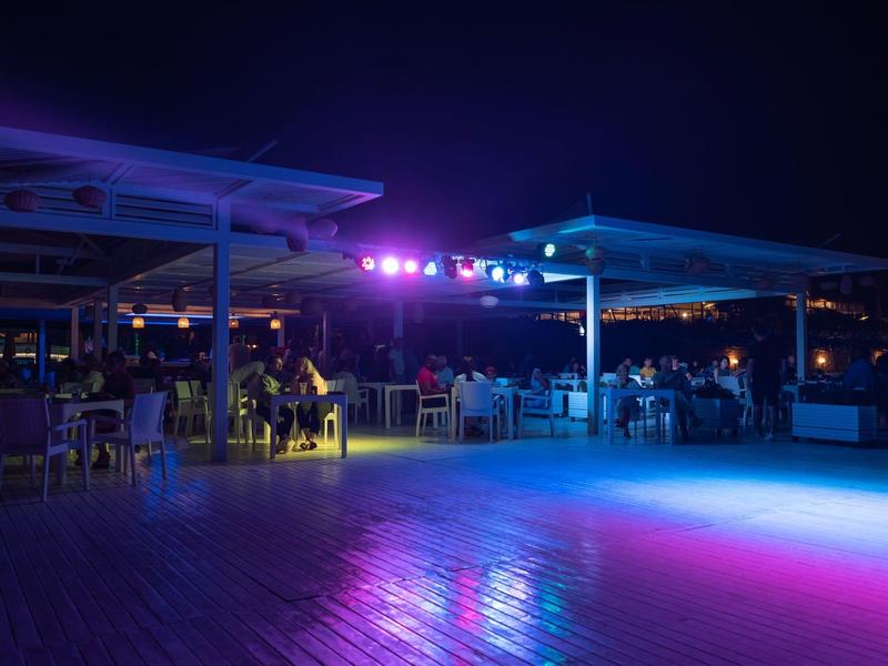 Evening scene on a hotel terrace with colorful lights and guests.