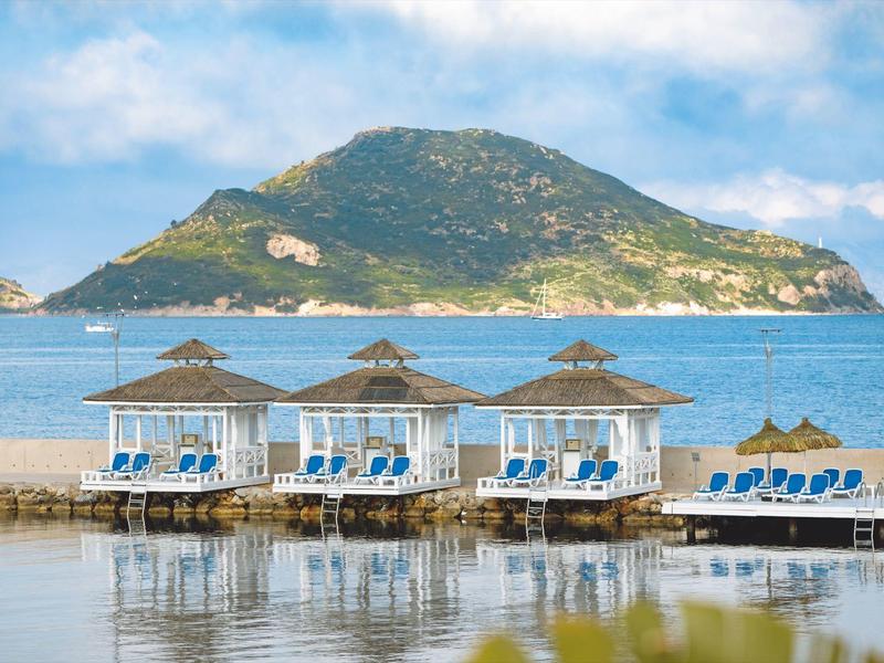 Three sunbeds with umbrellas on dock in front of island in the sea