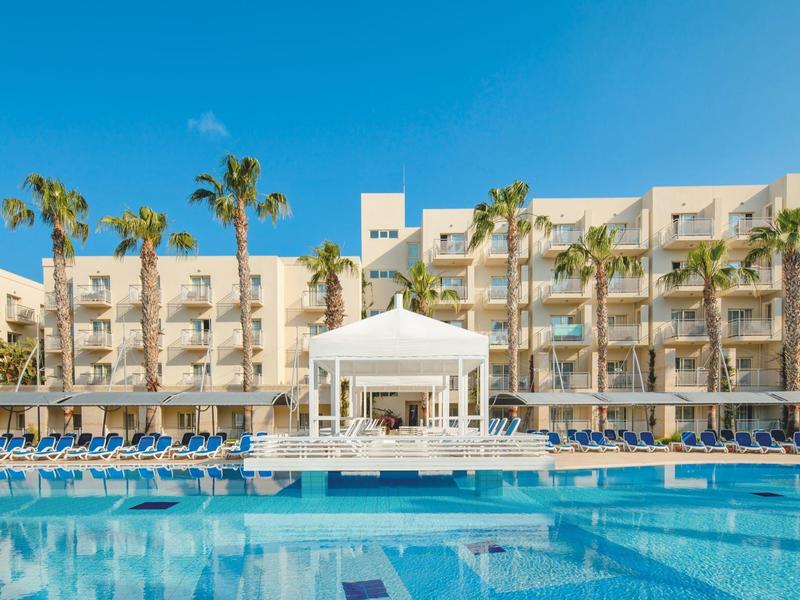 Hotel building with pool and palm trees under clear blue sky