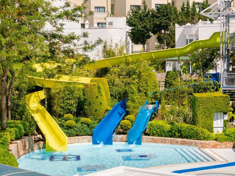 Several colorful water slides leading into a pool in a hotel garden.