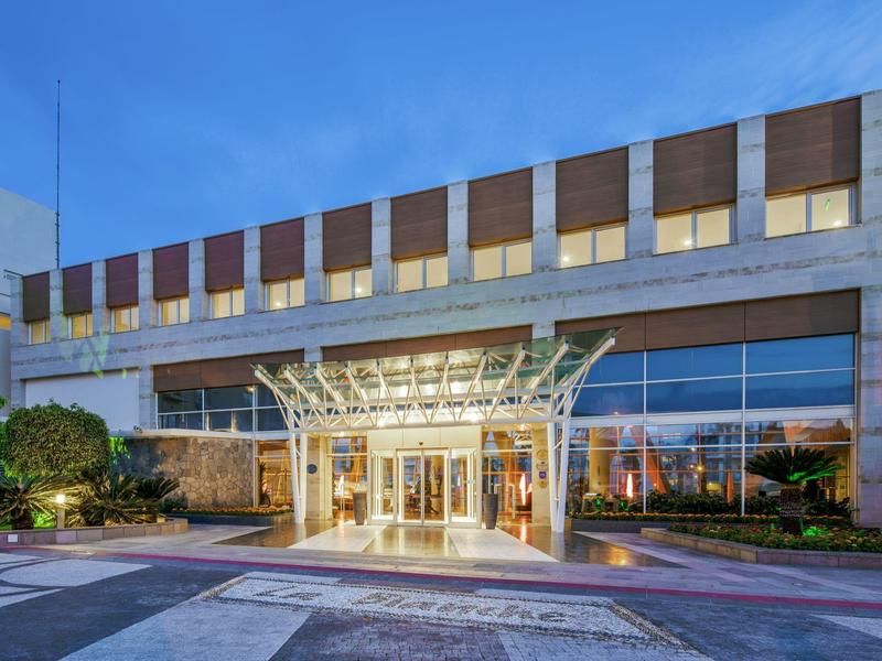 Modern hotel entrance with glass canopy and large windows at dusk.